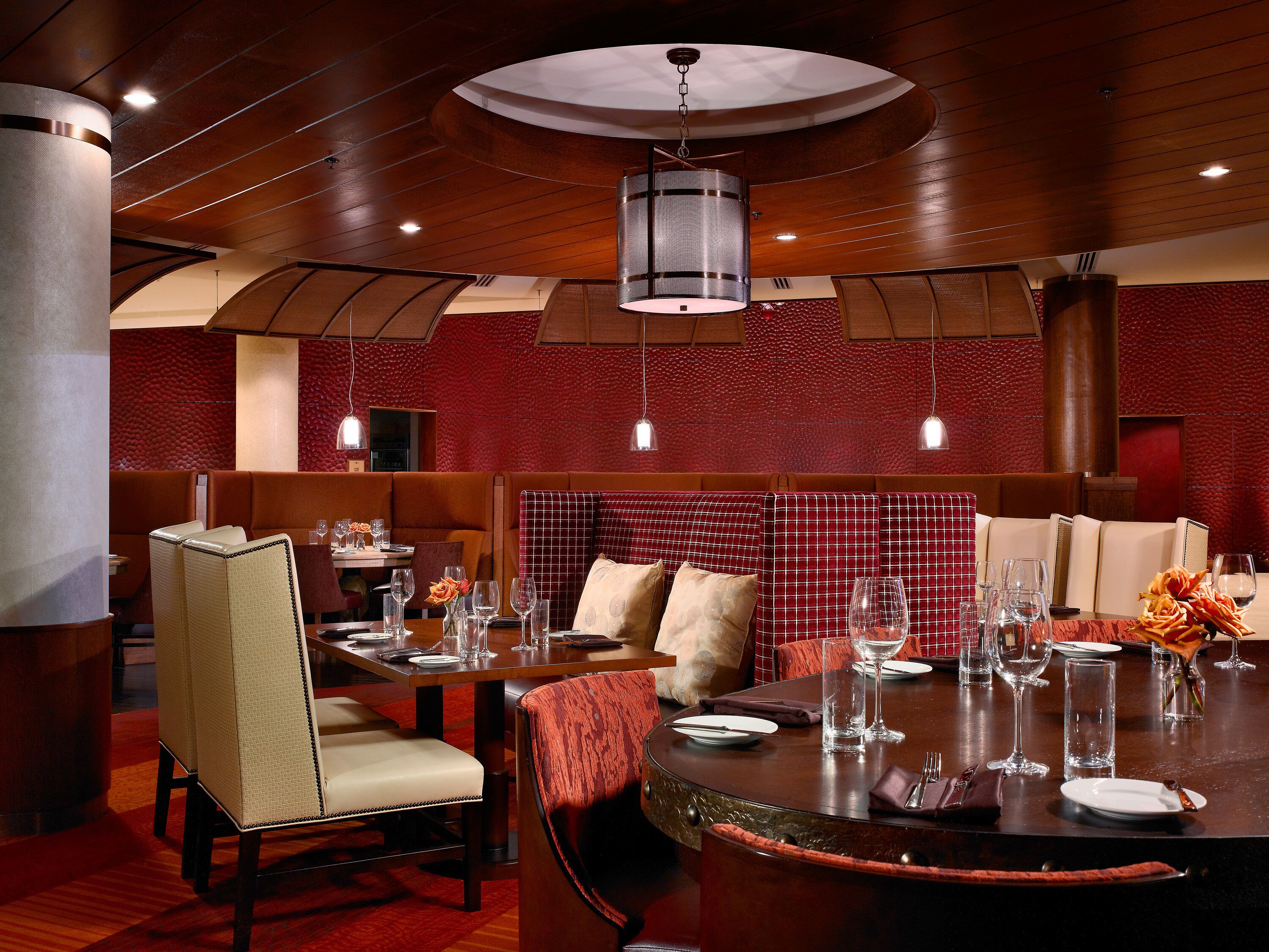 Un restaurante con cabinas y mesas, techo de madera y paredes rojas con textura.