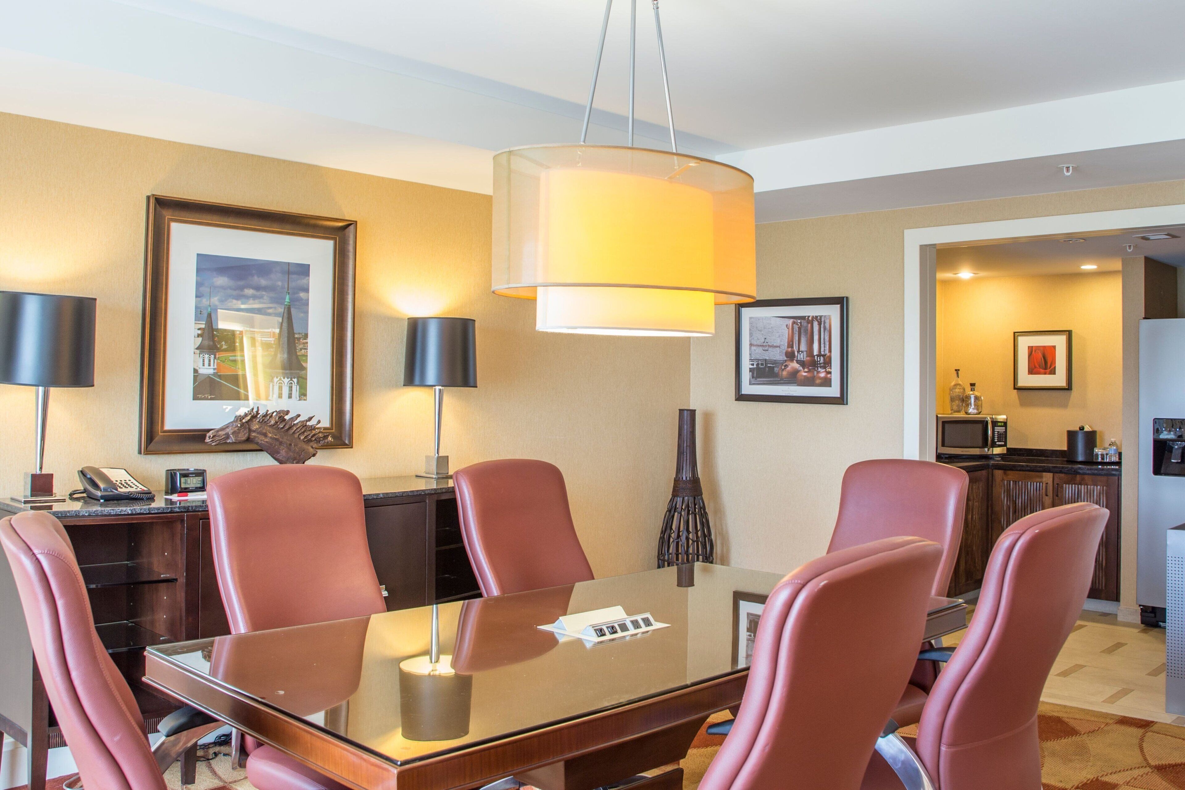 Uma área de refeições de hotel com uma mesa de vidro, cadeiras vermelhas e uma luminária grande pendurada.