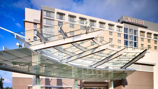 L’entrée d’un hôtel Marriott, avec un auvent moderne en verre, une façade en briques et un ciel dégagé.