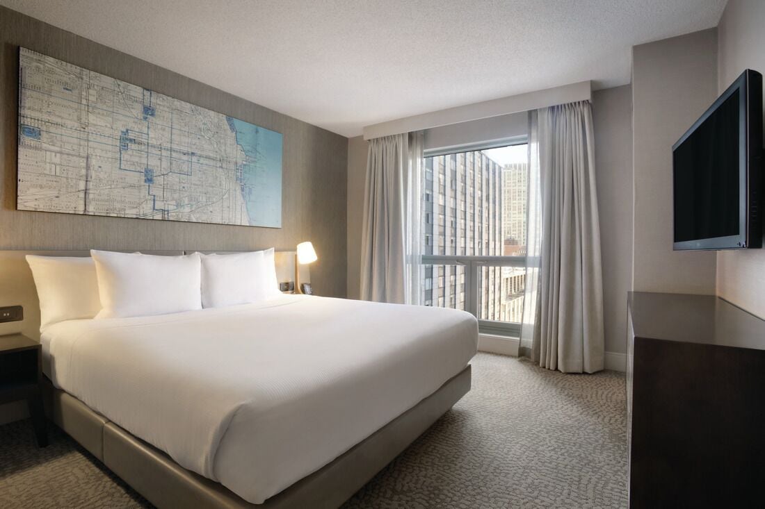 Une chambre d’hôtel avec un grand lit, un téléviseur à écran plat, une carte accrochée au mur et une fenêtre avec des rideaux.