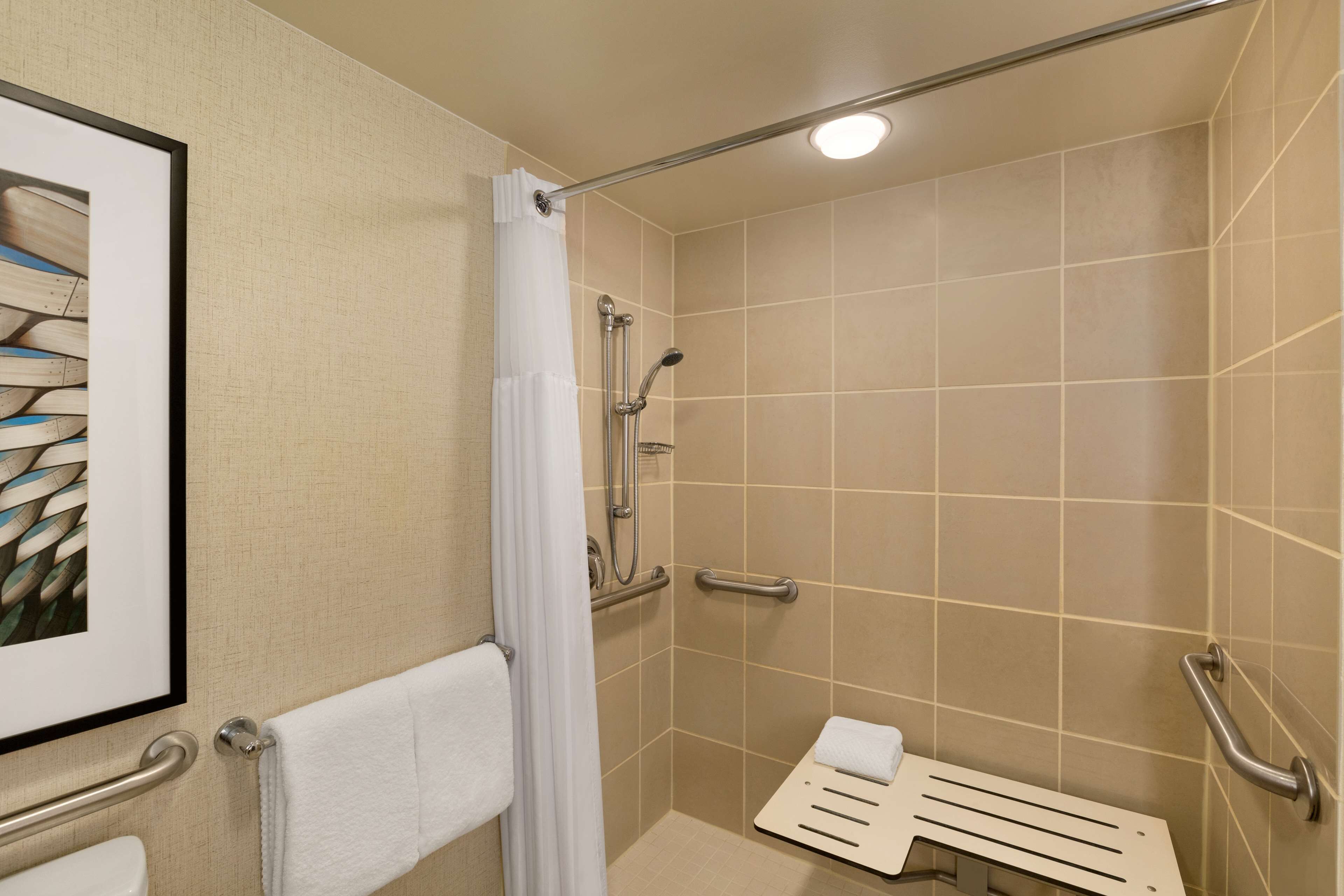 A shower area with a white shower curtain, grab bars, and a towel rack.