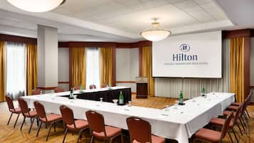 Un salón de conferencias con una larga mesa, sillas, una pantalla de proyector y un atril con el logotipo de Hilton.