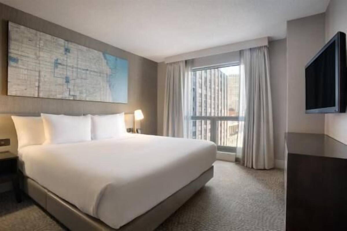 A hotel room with a large bed, a flat-screen TV, a window with curtains, and a map on the wall.