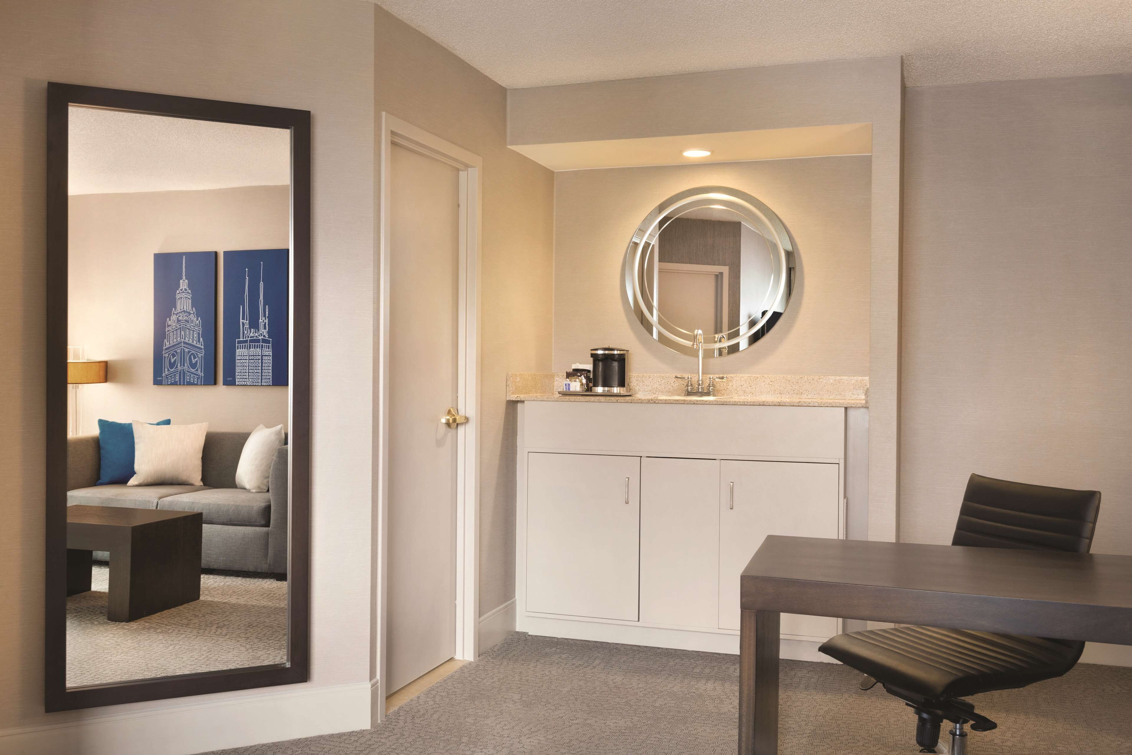 Une chambre d’hôtel équipée d’une table à manger, d’une chaise, d’un canapé avec des coussins, d’une machine à café et d’un miroir au-dessus du lavabo.