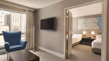 Habitación de hotel con un ventanal grande, un televisor de pantalla plana, un sillón azul, una cama, una mesita de noche con lámparas y un mapa en la pared.