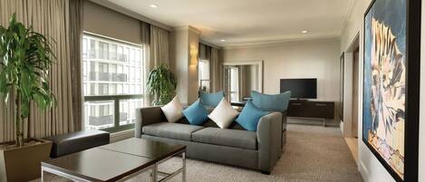 A spacious living room with a grey sofa, a coffee table, and two potted plants.