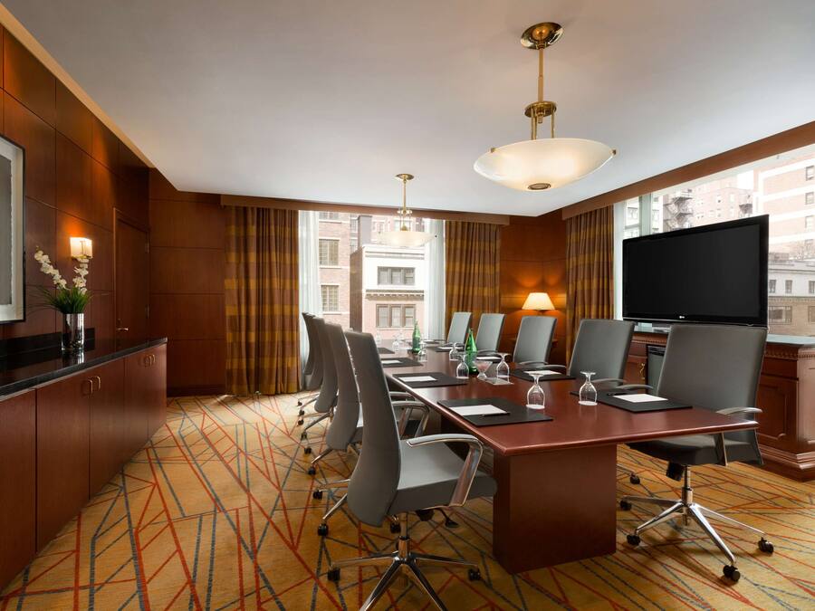 A conference room with a long table, chairs, a TV, and a city view through large windows.