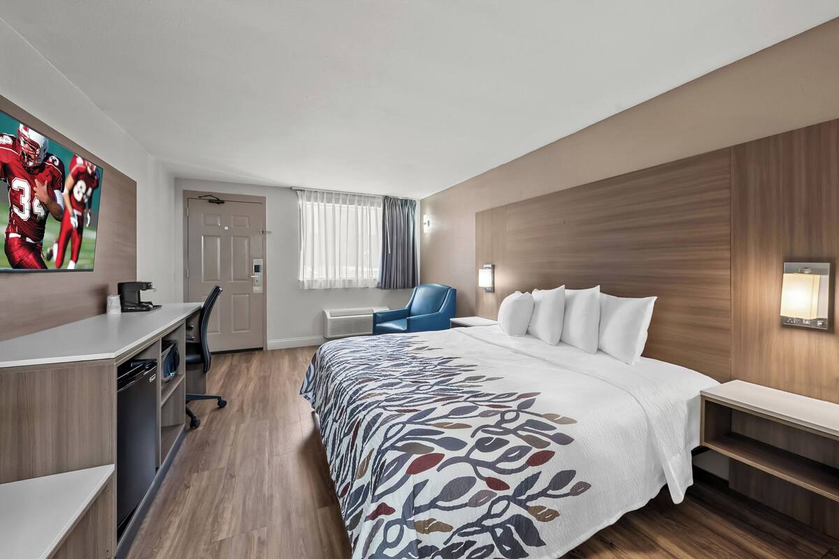 A hotel room with a bed, desk, chair, and a large window with curtains.
