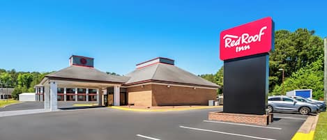 A Red Roof Inn with a clear sky, parking lot, and a building with a red roof and brick facade.