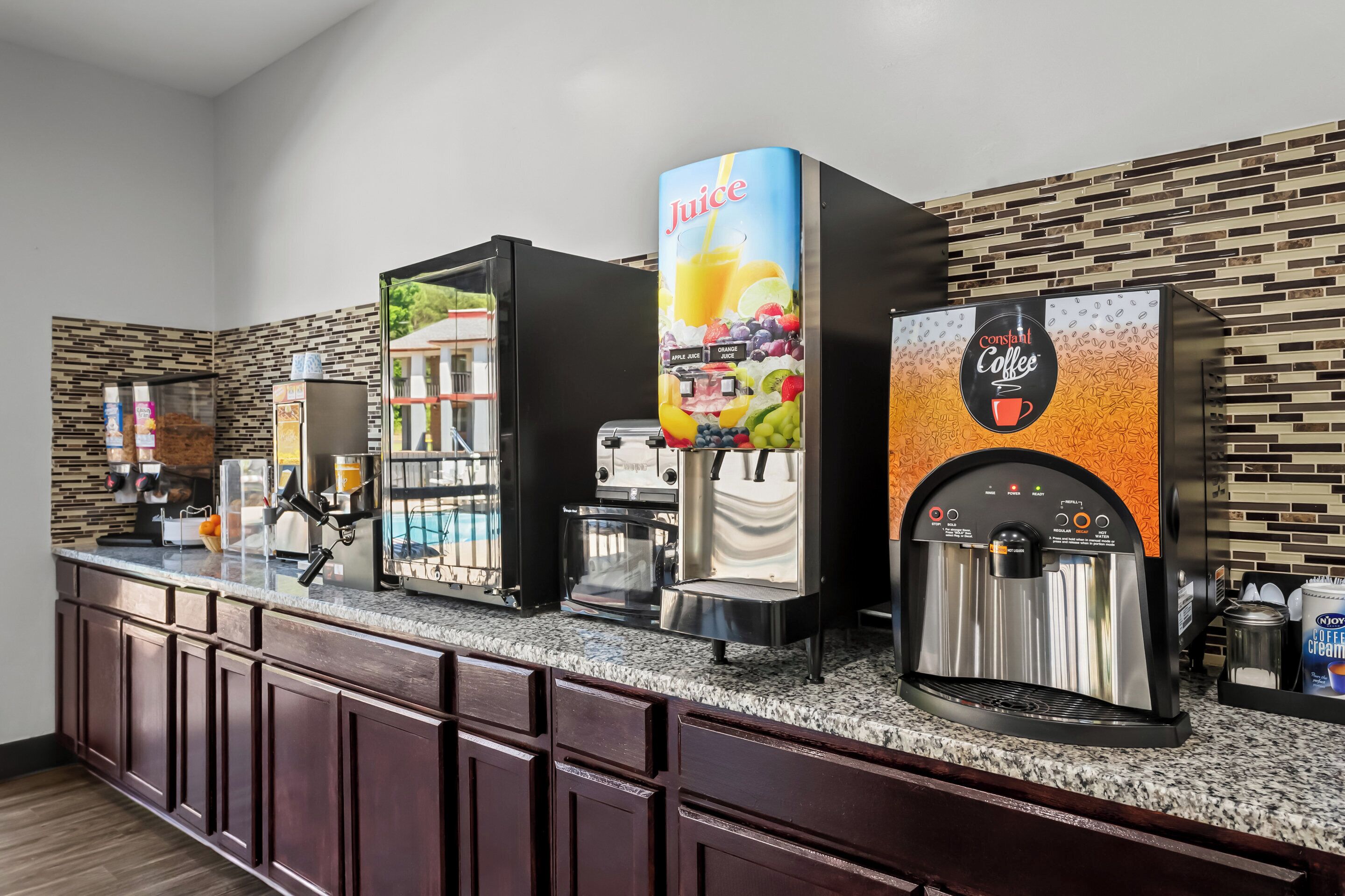 A self-service beverage station with multiple dispensers, including juice and coffee options, in a modern hotel setting.