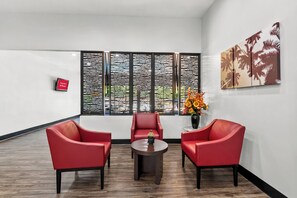A modern room with a wooden floor, red chairs, a small table, and a decorative wall piece. - Red Roof Inn Sanford (Sanford)