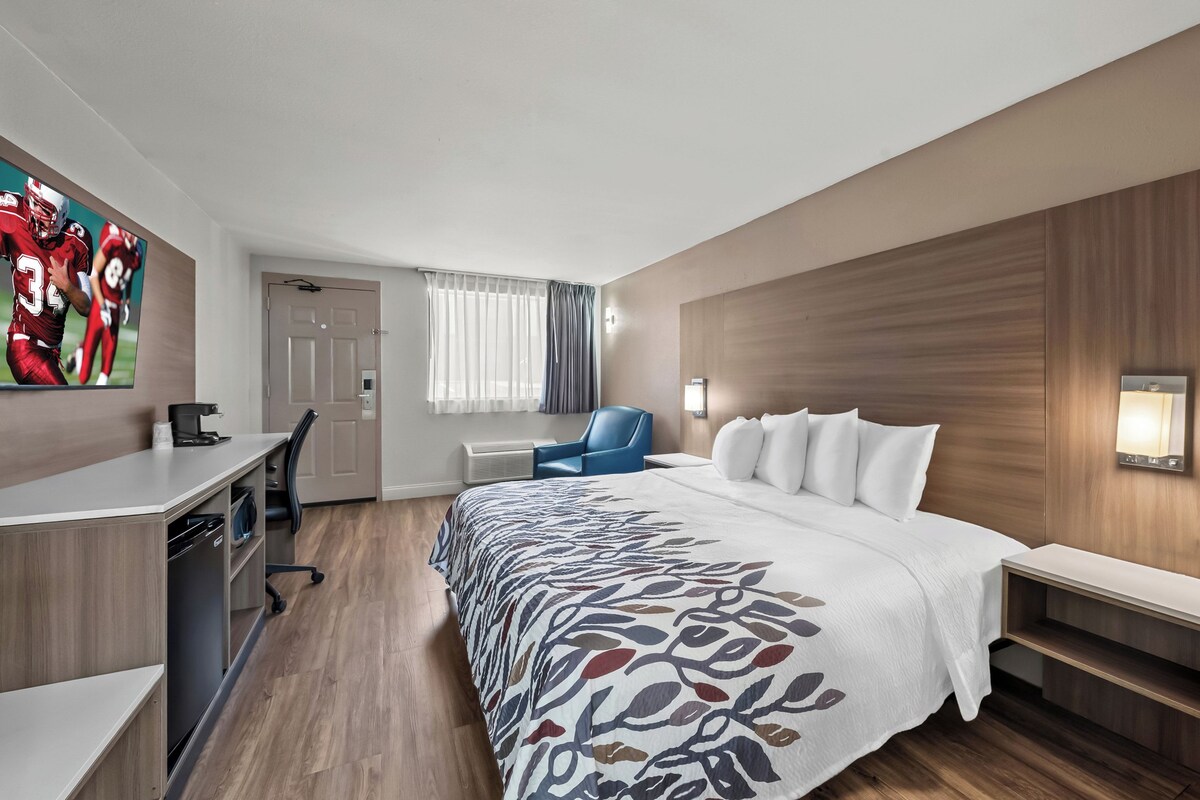 Een hotelkamer met een bed, bureau, stoel en een groot raam met gordijnen.