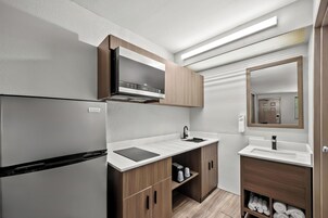 Cocina compacta con microondas integrado, pileta y armarios de madera.