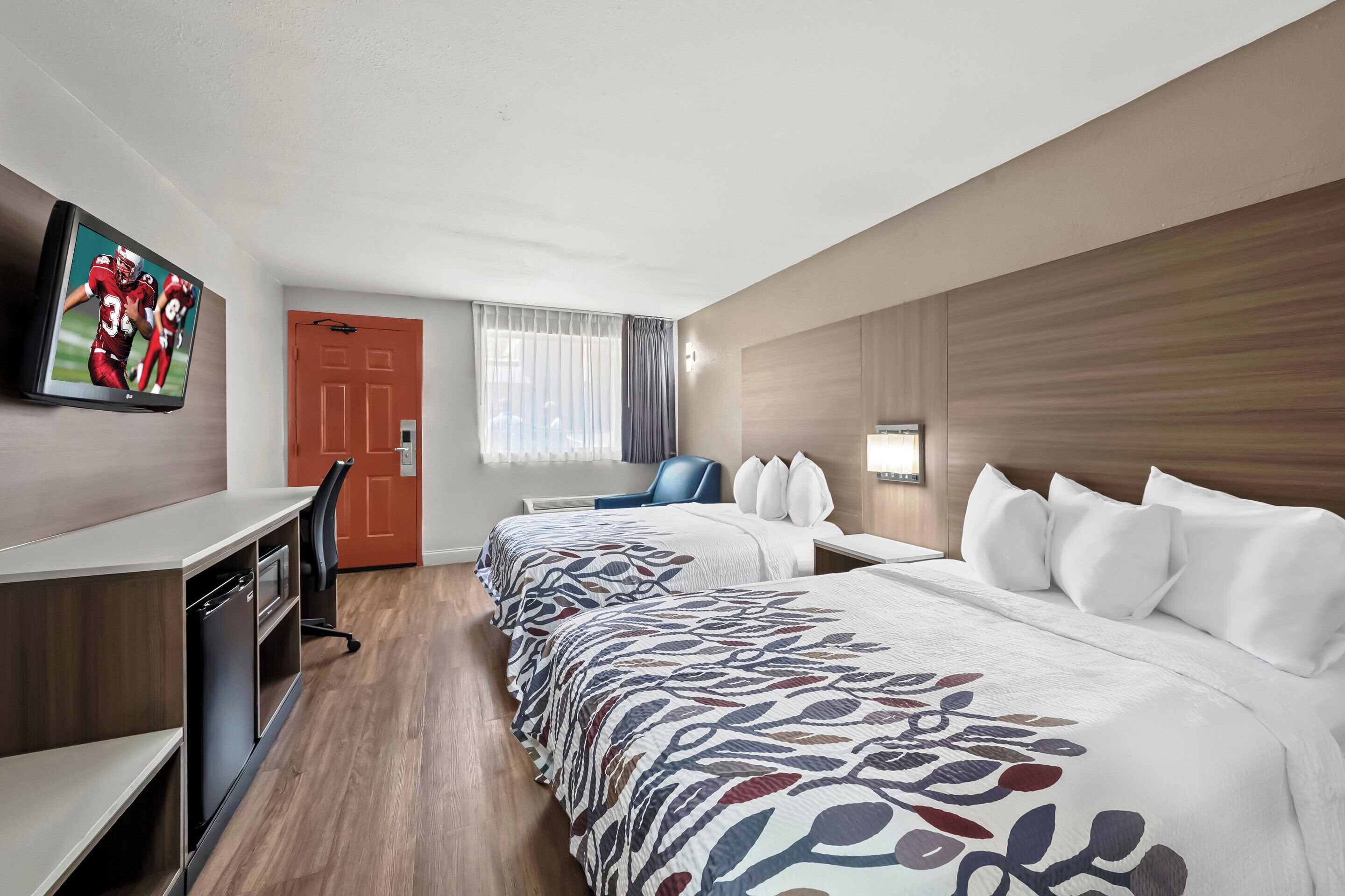 A hotel room with a bed, a desk, a chair, a TV, and a door.