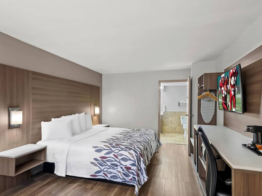 Een hotelkamer met een bed, nachtkastje, bureau met stoel, televisie en een douche.