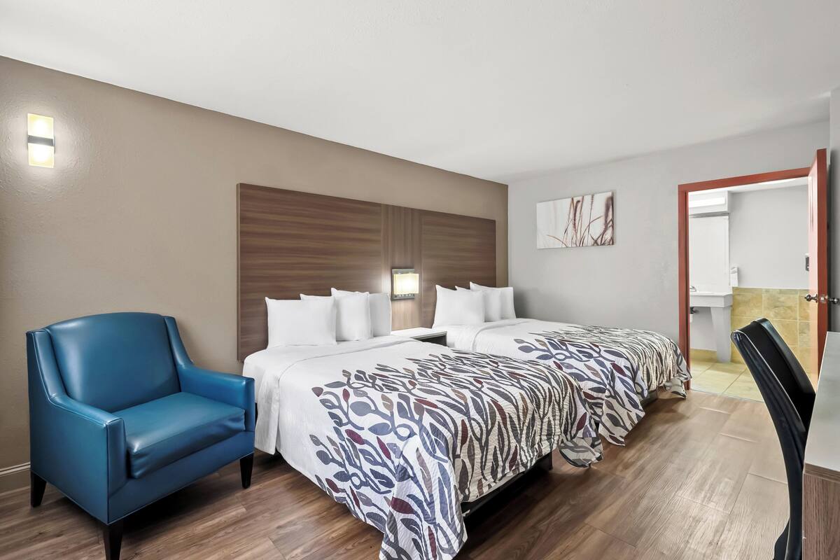 A hotel room with a bed, a chair, a bedside table, and a wall-mounted light.