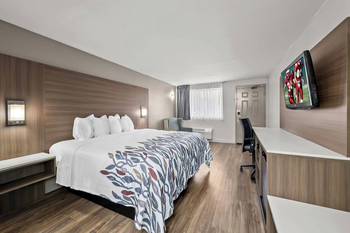 A modern hotel room with a large bed, a desk, and a television mounted on the wall.