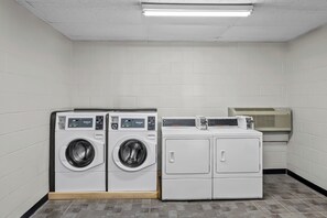 A laundry room with two front-loading washers and dryers, a ventilation unit, and a tiled floor. - Red Roof Inn Sanford (Sanford)