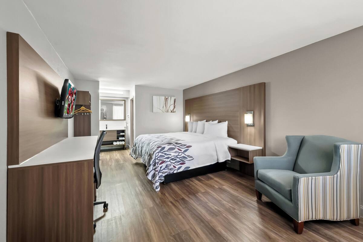 A modern hotel room with a large bed, a desk, a chair, and a TV mounted on the wall.