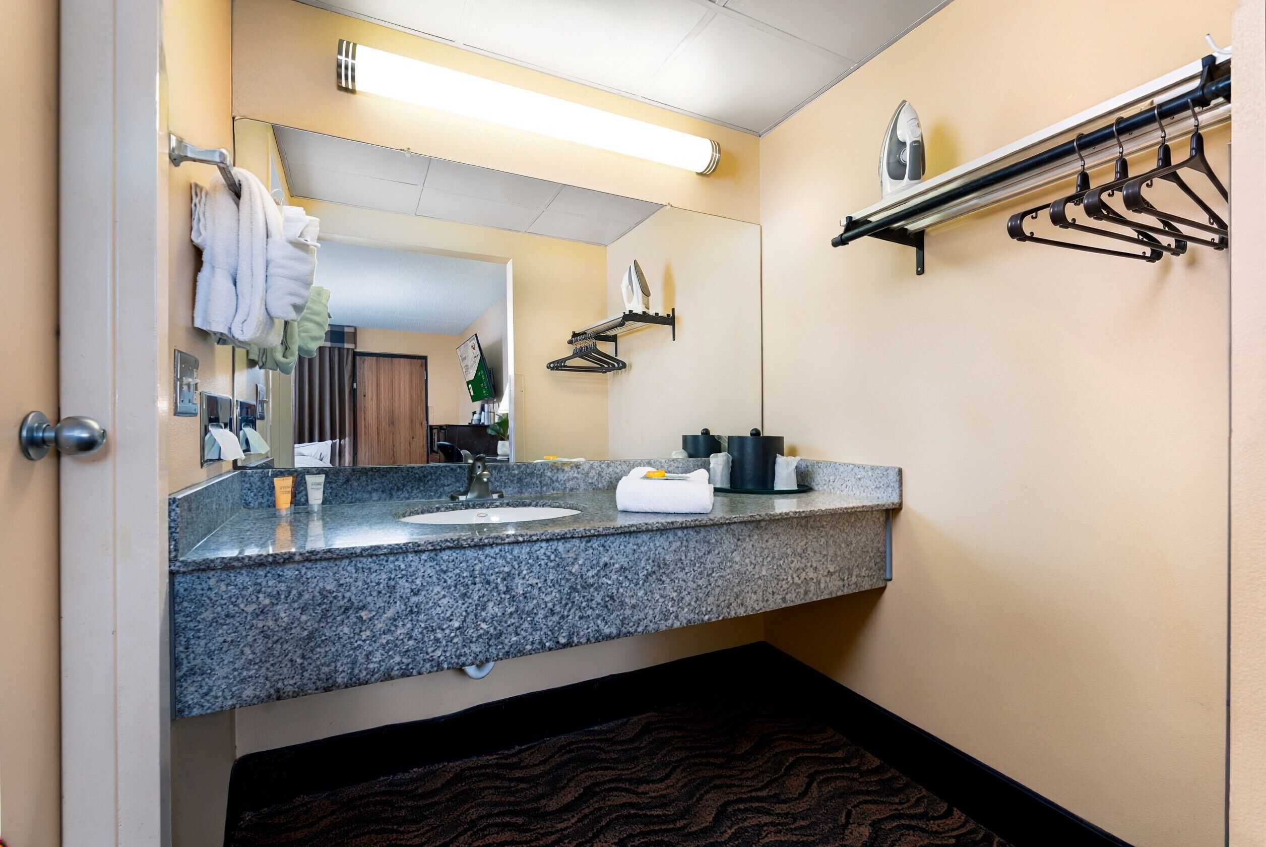 A hotel bathroom with a granite countertop, a sink, a mirror, a towel rack, and a shower area.