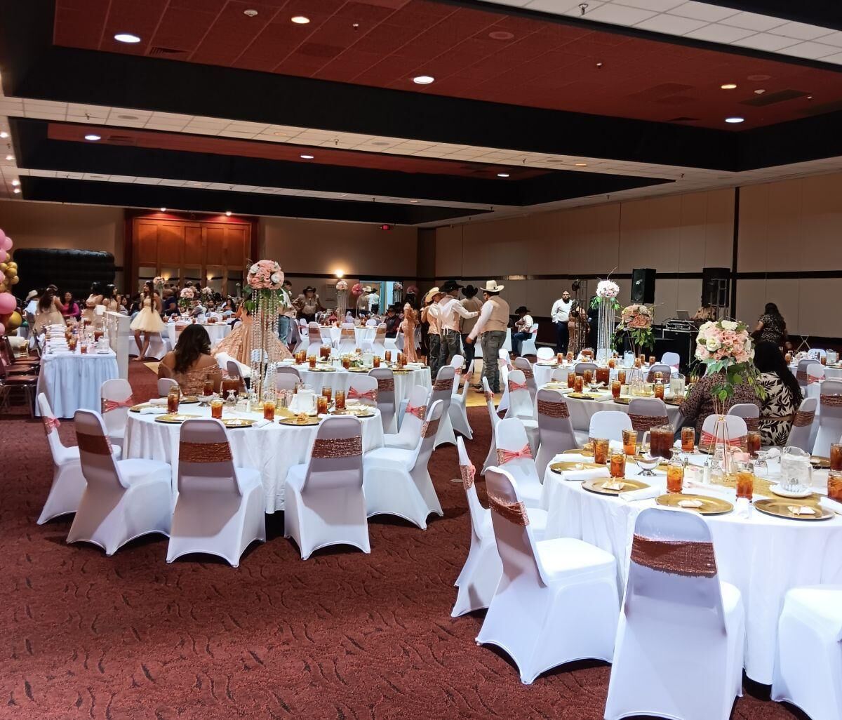 A banquet hall with round tables set for a formal event, featuring white tablecloths and chairs with pink sashes.