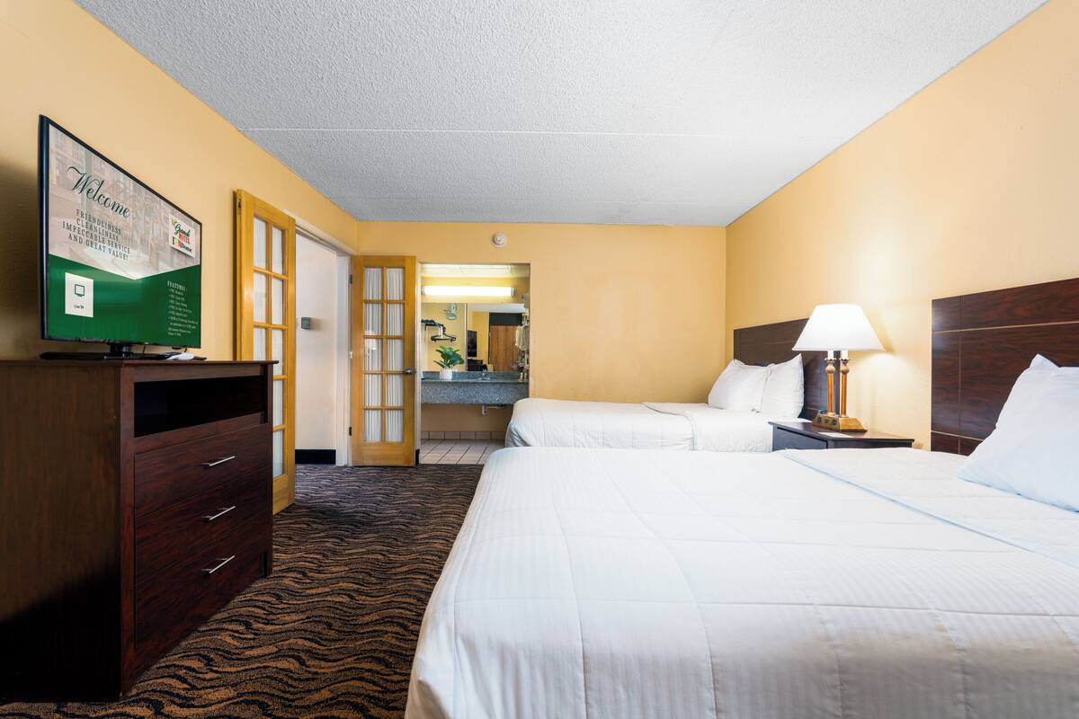 A hotel room with two beds, a TV, a desk, and a bathroom visible through an open door.