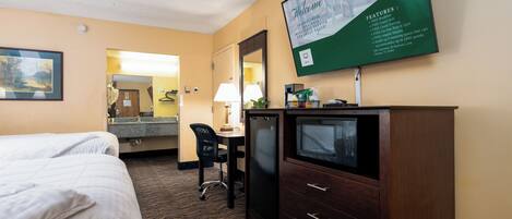 A hotel room with two beds, a desk with a chair, a television, and a large informational sign on the wall.