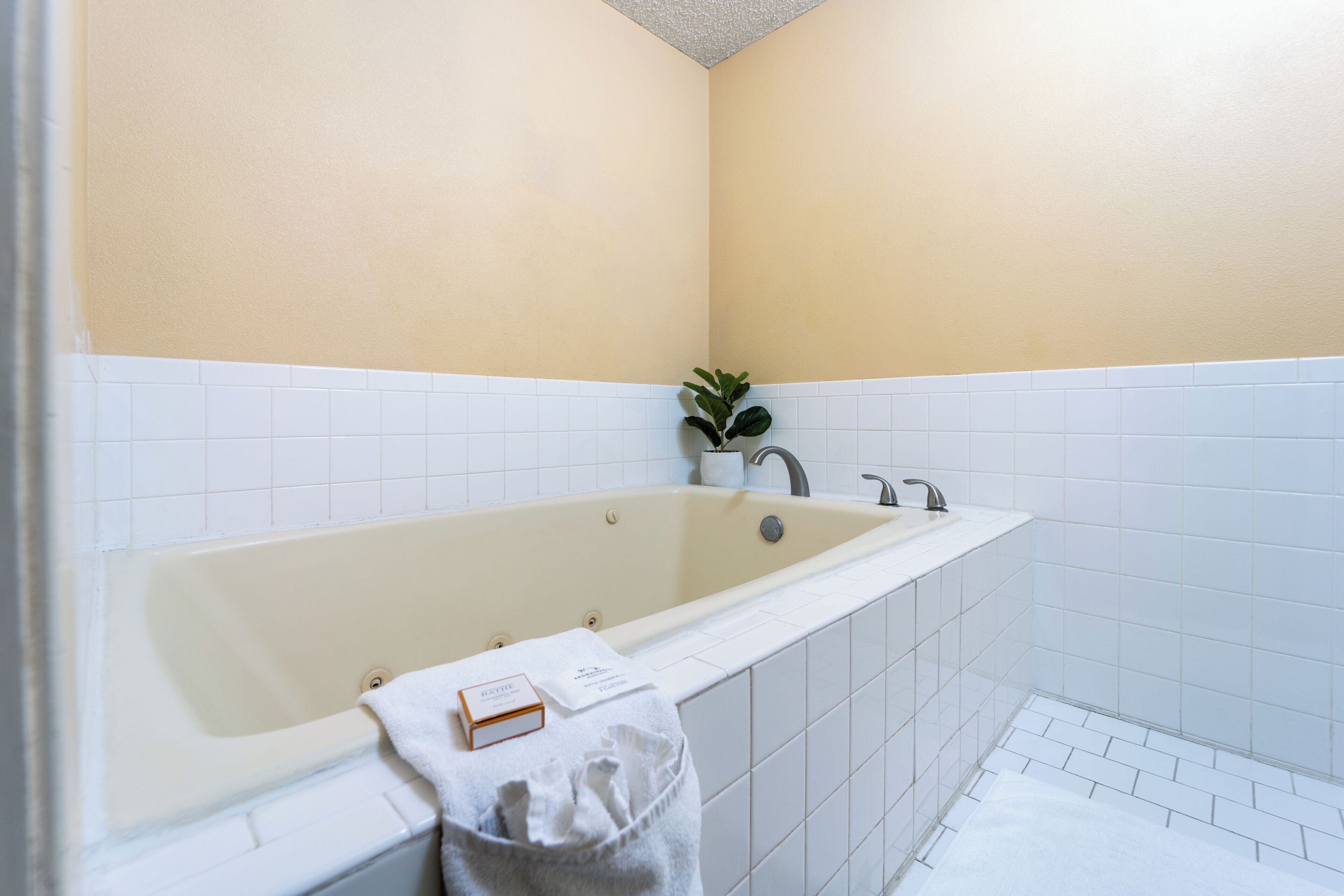 A modern bathroom with a beige bathtub, white tiled walls, and a small potted plant.