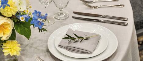 A table set with white plates, silverware, and a folded napkin with a green leaf.