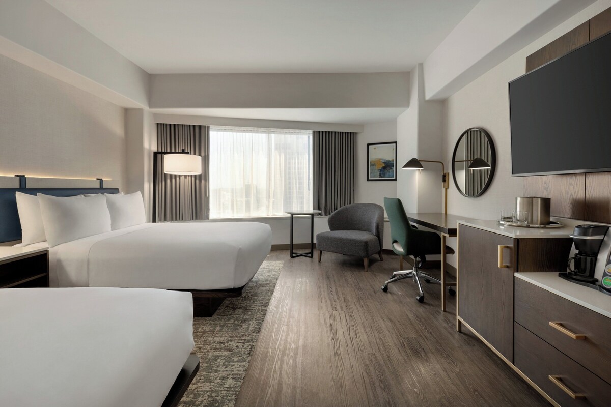 A hotel room with two beds, a desk, a chair, a TV, and a coffee maker.