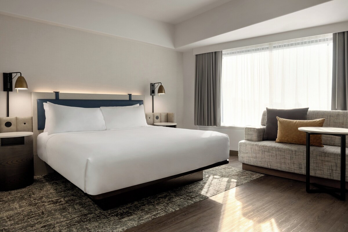 A modern hotel room with a large bed, a sofa, a small table, and two bedside lamps.