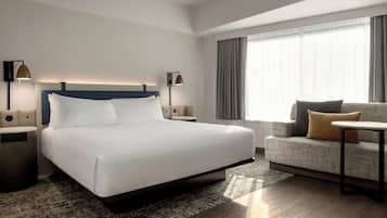 A modern hotel room with a large bed, a sofa, a small table, and two bedside lamps.