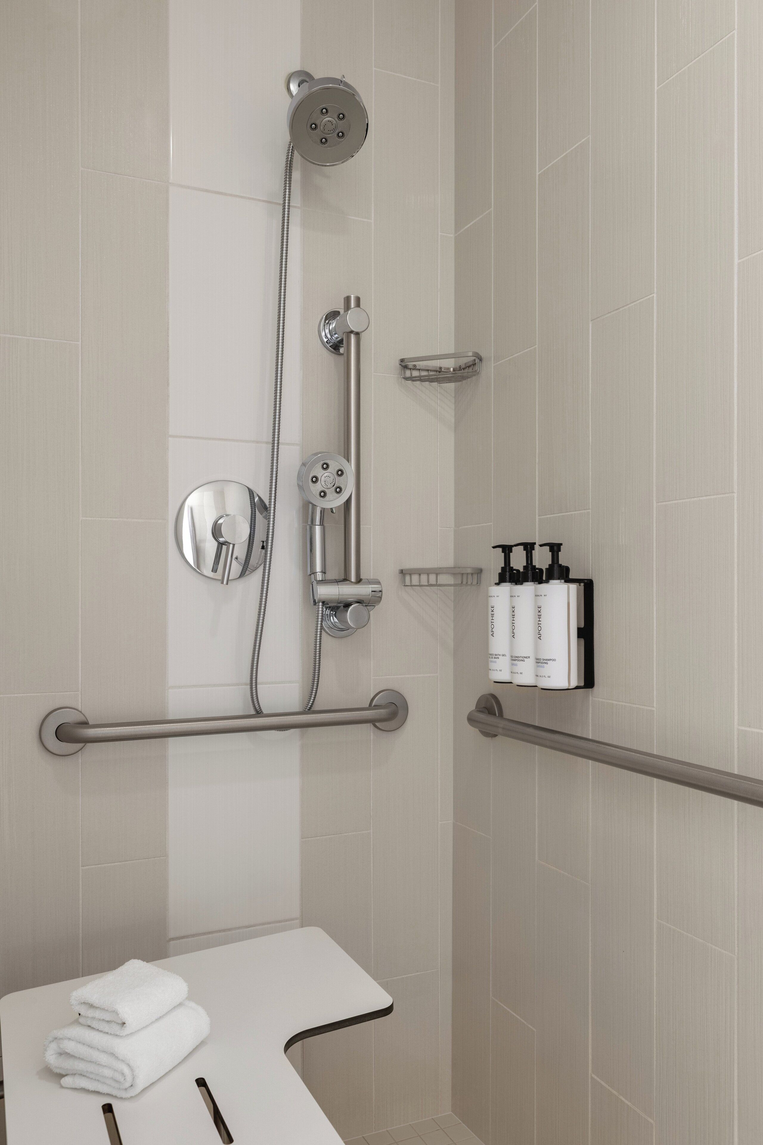 A modern bathroom with a shower, grab bars, and a towel rack.