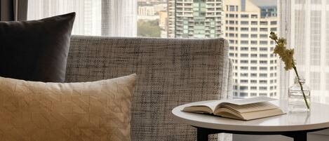 A hotel room with a view of the Seattle skyline, including the Space Needle, a sofa with a pillow, a small table with an open book and a vase with flowers.