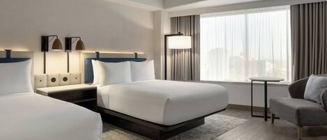 Una habitación de hotel con dos camas, un escritorio, una silla, un ventanal grande con cortinas y una lámpara.