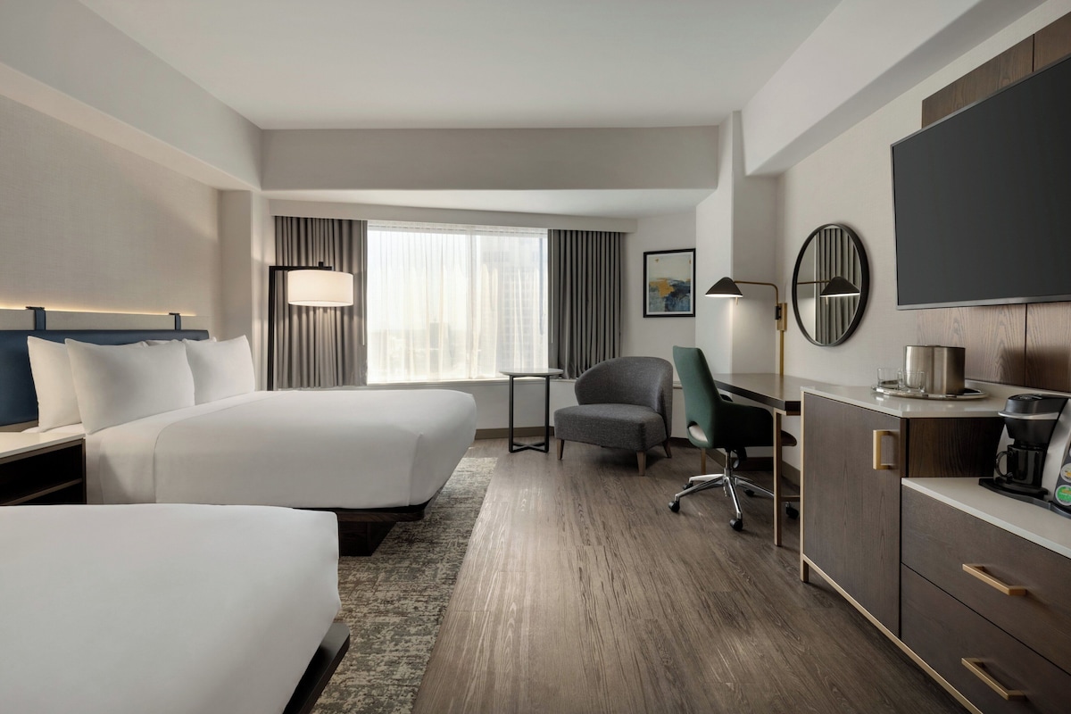A hotel room with two beds, a desk, a chair, a TV, and a coffee maker.