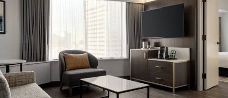 Una habitación de hotel moderna con sofá, mesa de centro, televisor y escritorio con cajones.