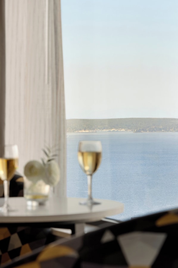 Una mesa con una copa de vino y una bandeja de frutas, con vistas a un cuerpo de agua.