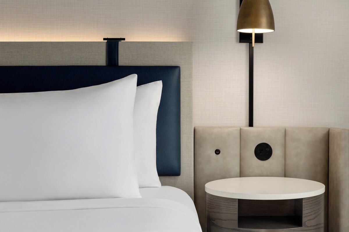 A modern hotel room with a bed, a round table, and a lamp.