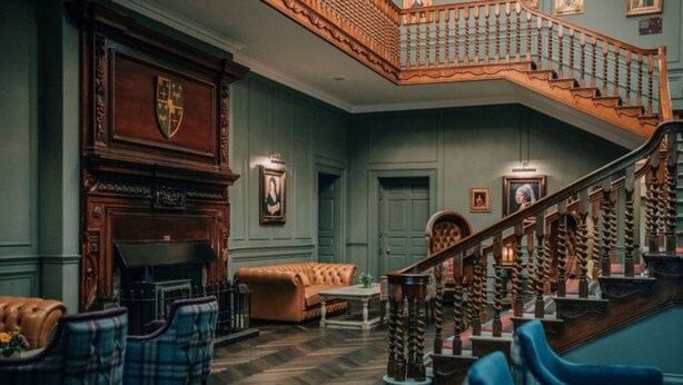 A grand lobby with a wooden staircase, a fireplace, and a leather sofa. - Blackwell Grange Hotel (Darlington)