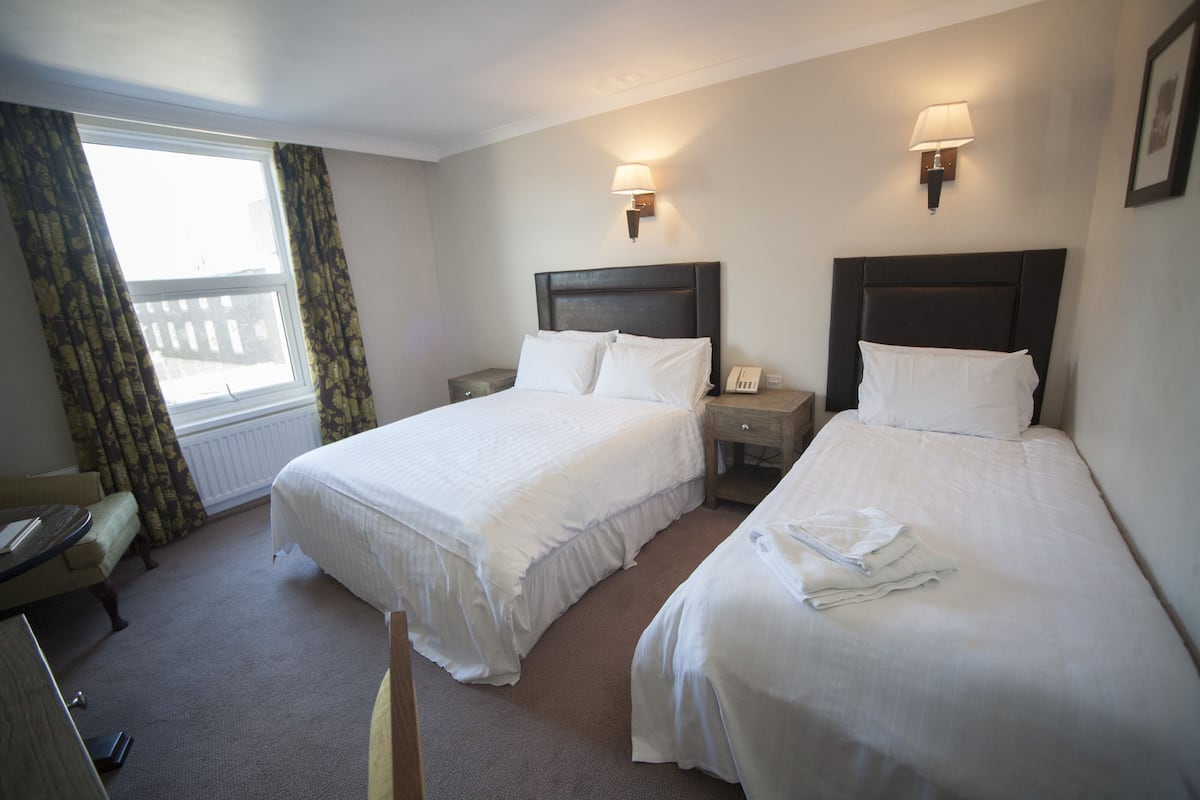 Quarto de hotel com duas camas, uma escrivaninha, uma cadeira e uma janela com cortinas.