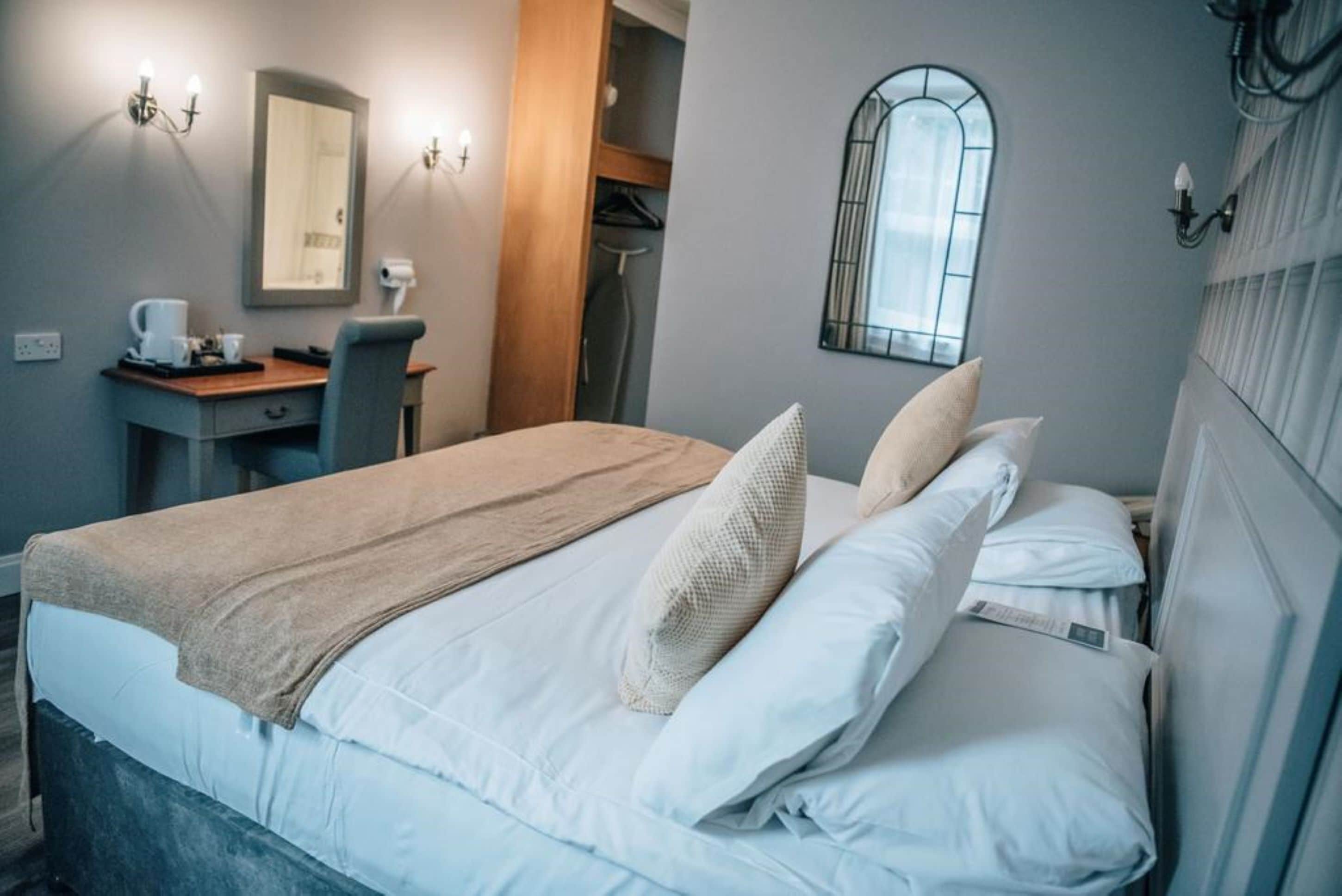 A neatly arranged bedroom with a bed, bedside table, and a mirror.