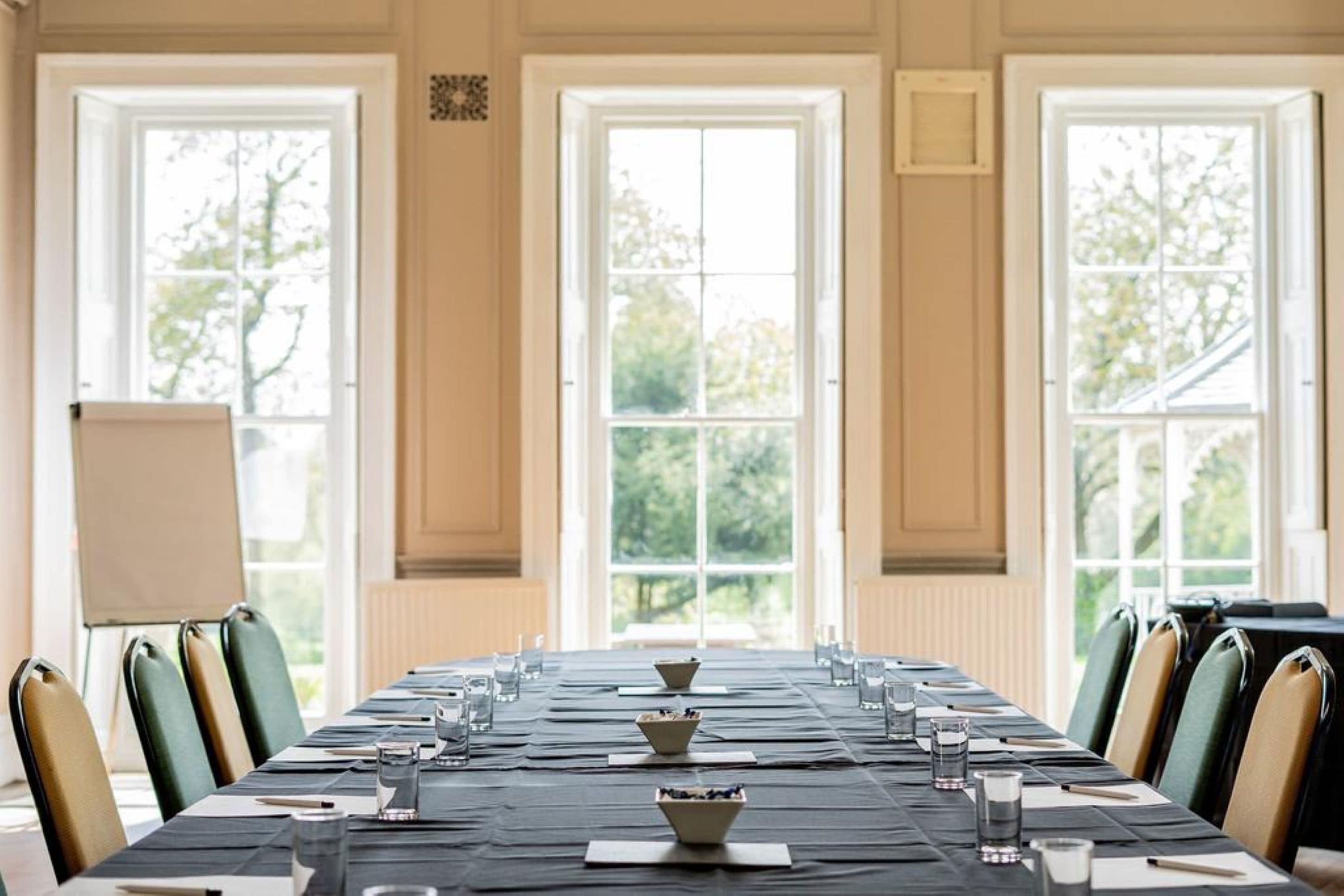 A conference room with a long table set for a meeting, large windows, and a view of trees.
