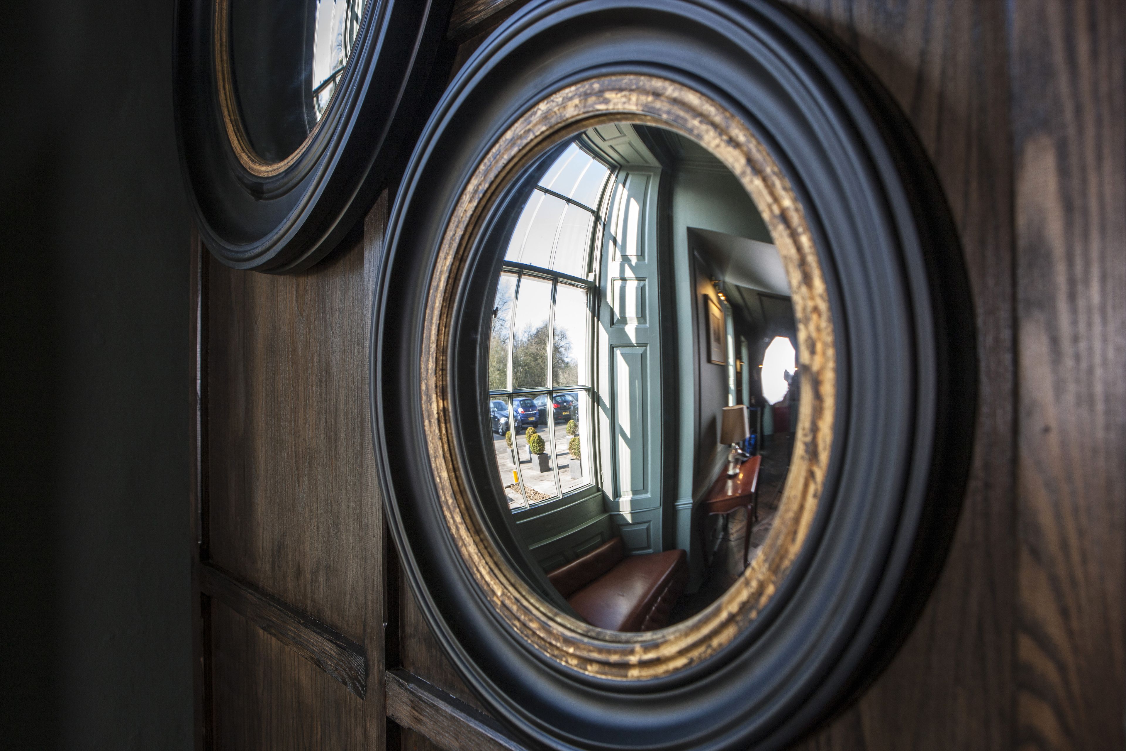 Vista a través de una ventana circular con marco de madera, que refleja el interior de un edificio y un estacionamiento exterior.