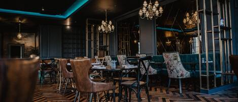 A restaurant interior with wooden flooring, tables, chairs, and hanging chandeliers.