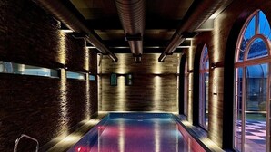 A modern indoor swimming pool with a wooden ceiling and brick walls, large arched windows, and a clear view outside. - Blackwell Grange Hotel (Darlington)