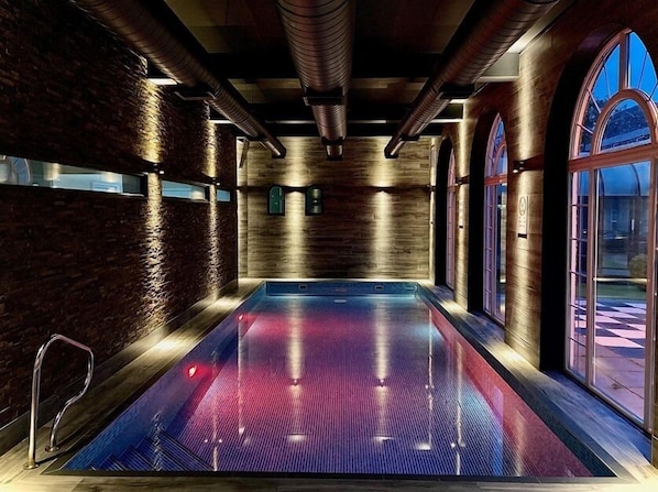 Una piscina interior moderna con techo de madera y paredes de ladrillo, ventanas arqueadas grandes y vistas despejadas al exterior.