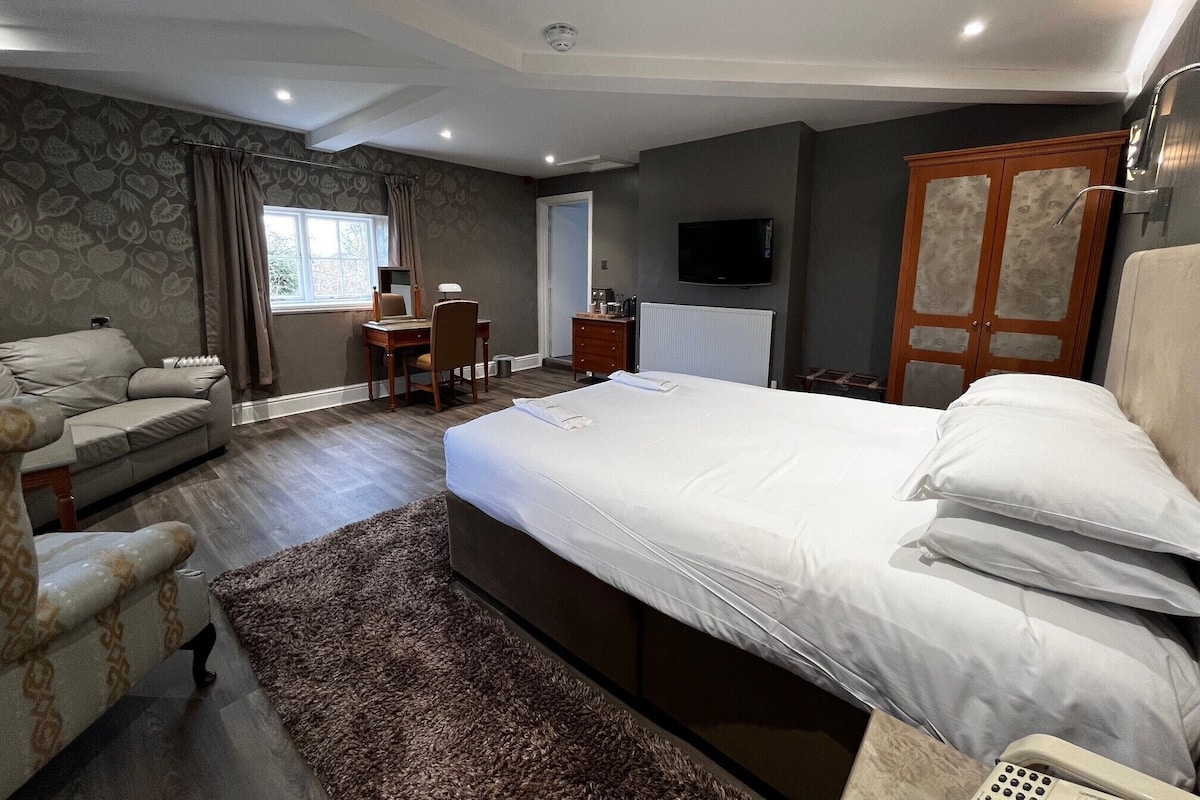 Quarto de hotel moderno com uma cama grande, um sofá, uma escrivaninha e uma televisão.