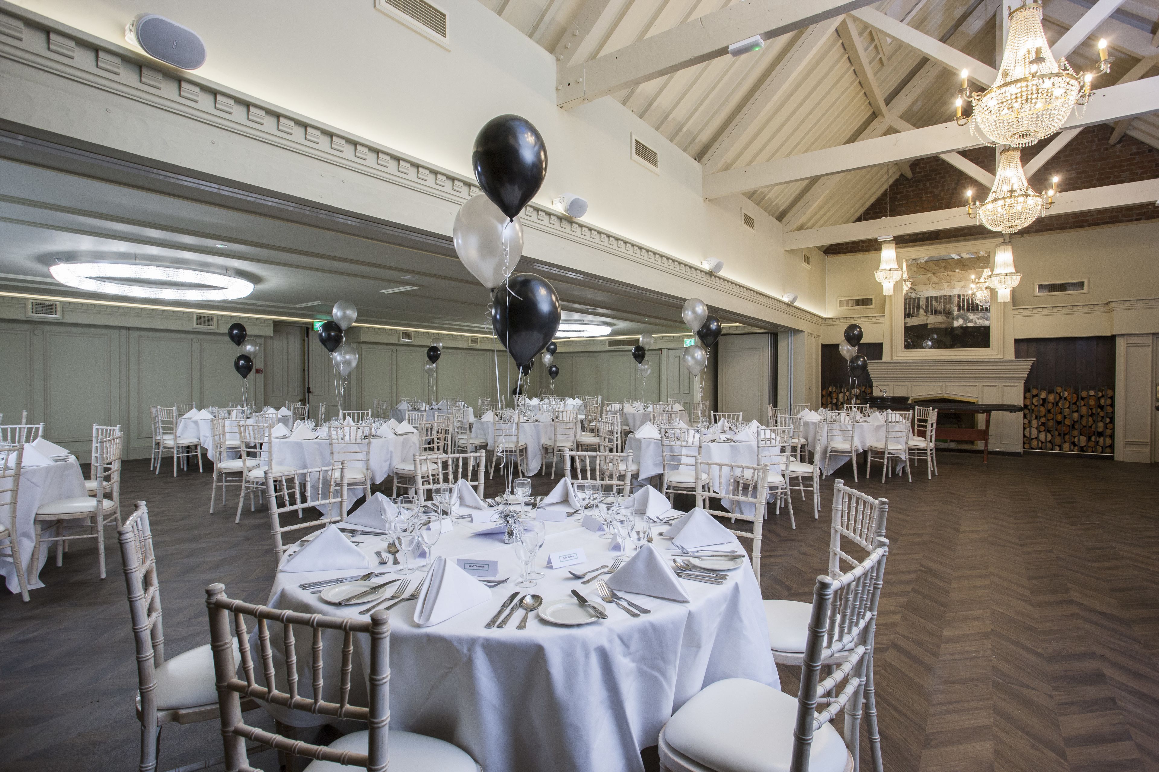 A banquet hall with round tables set for dining, white chairs, and chandeliers.