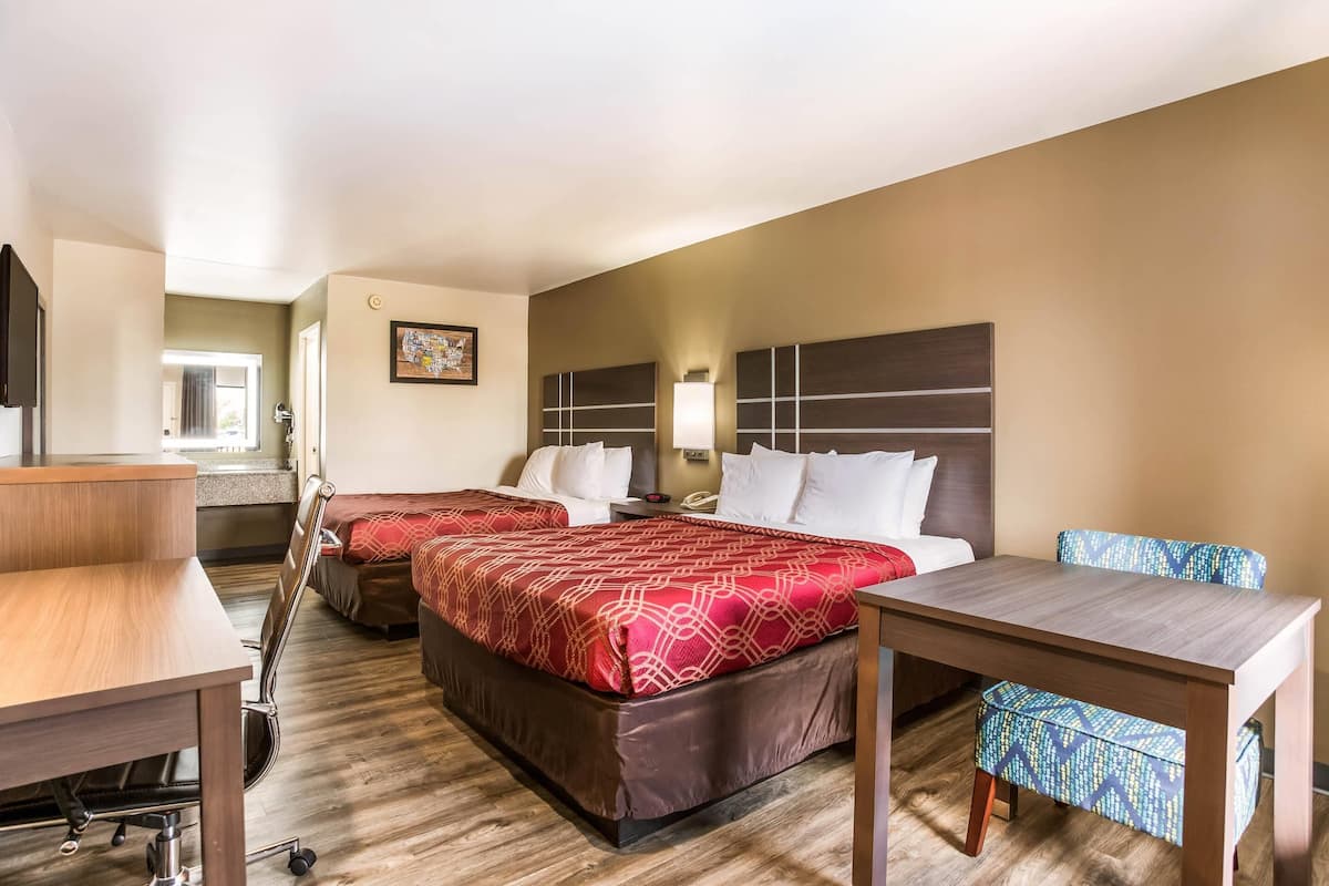 A hotel room with two beds, a desk, a chair, and a small table.